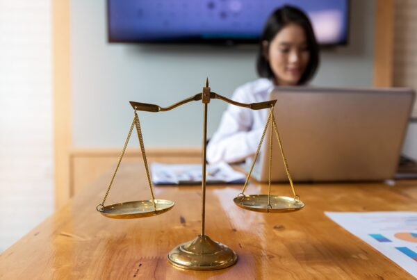 How to Choose the Best Legal Funding for Your Needs. Image of a woman working on a laptop with a legal scale in the foreground.